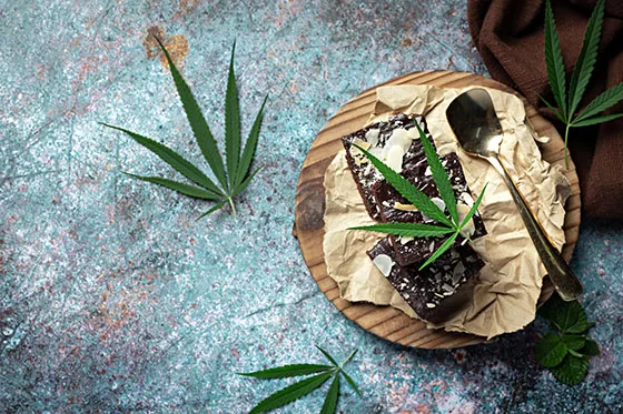 Cannabis leaves, edible brownies lying on a paper, with spoon.