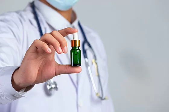 Medical professional holding a bottle of drops, possibly cannabis CBD extract.