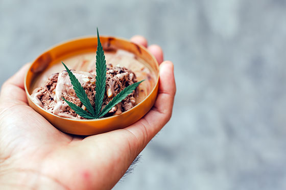 Cannabis-infused ice cream in a small container in hand, with a cannabis leaf.
