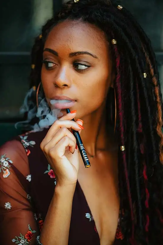 Young lady in braided hair using a vape.