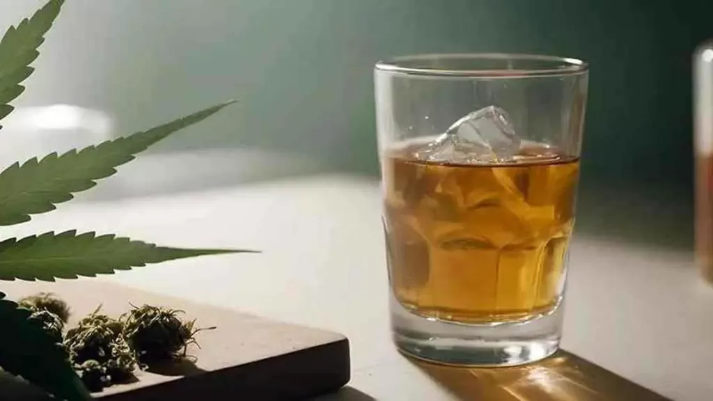 Image of a whiskey glass, with a cannabis leaf and flower near it.