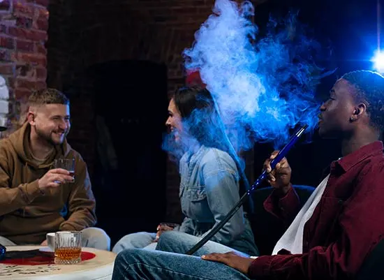 Two guys and a girl in what appears to be a lounge. One guy is using a hookah, while the other two have drinks.