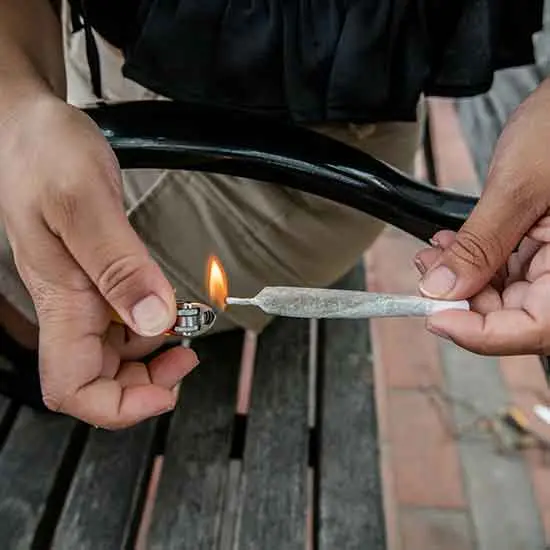 Closeup of a person lighting up a joint with a lighter on a wooden park bench,