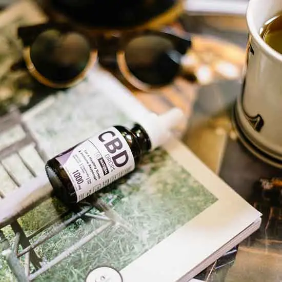 CBD Oil on table with sunglasses and a cup among other items.