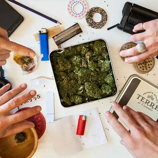 Multiple hands reaching for a box of cannabis flower.